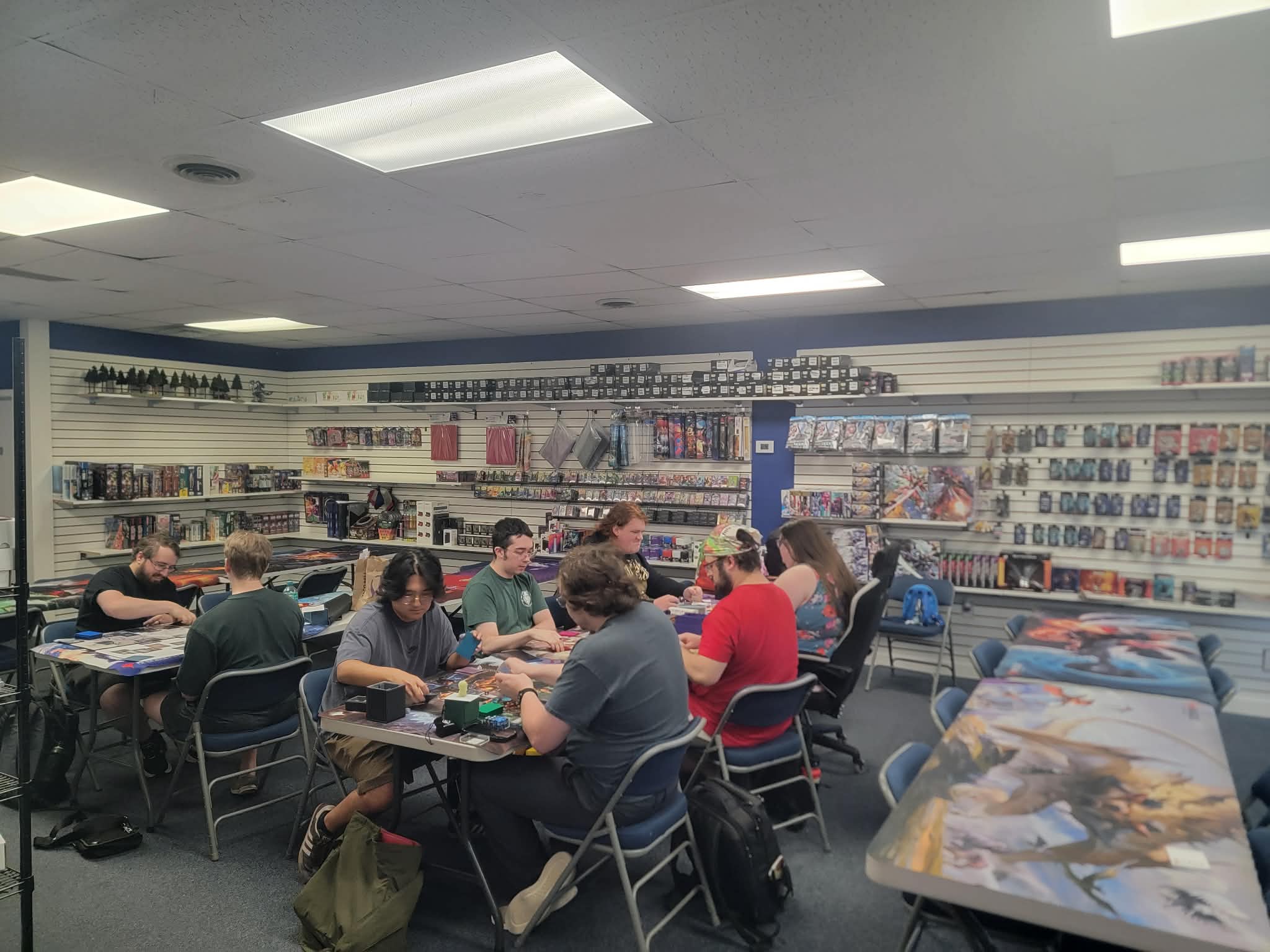 A wider view of the tournament room, playmats laid out on open tables in the foreground.